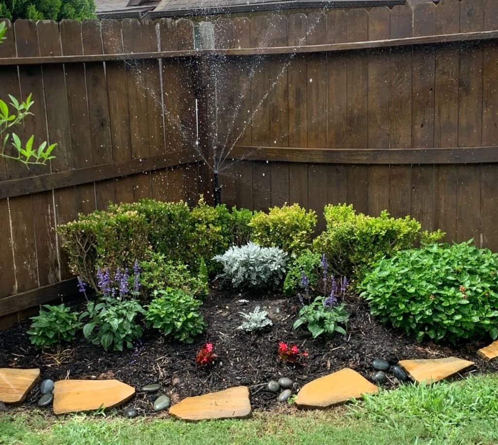 Sprinklers running in a flower bed in the corner of a green lawn