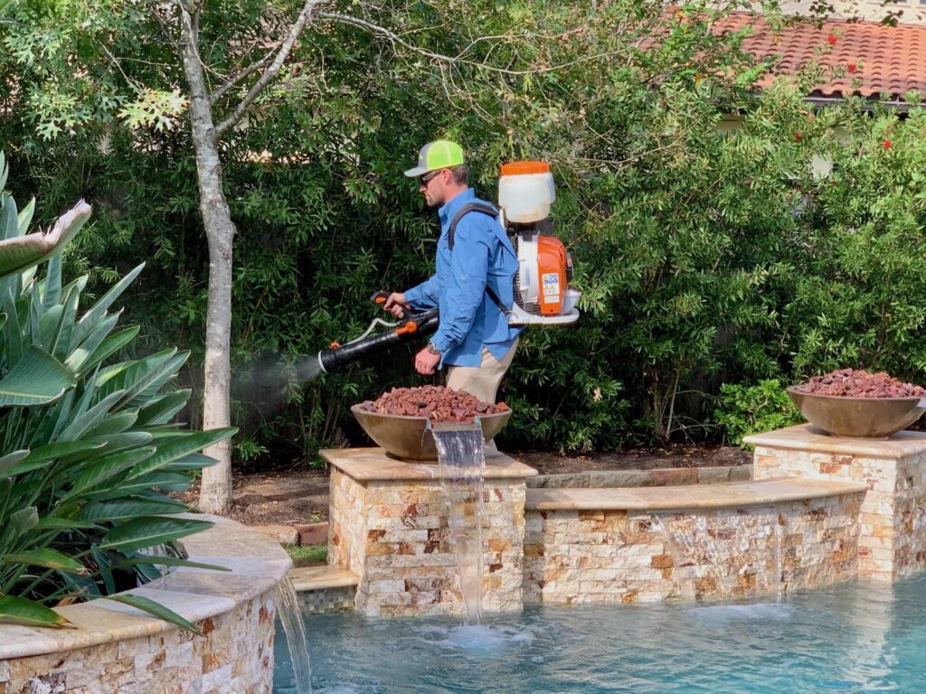 GreenGate technician applying a mosquito barrier spray on trees & shrubs near a pool in a backyard