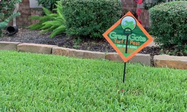 Close up of a Greengate sign in a green lawn next to a flower bed