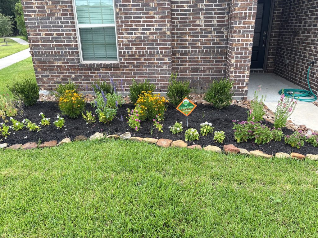 Close up photo of a flower bed along the front side of a brick home getting treated for lawn pest control including ant control services and chinch bug treatment