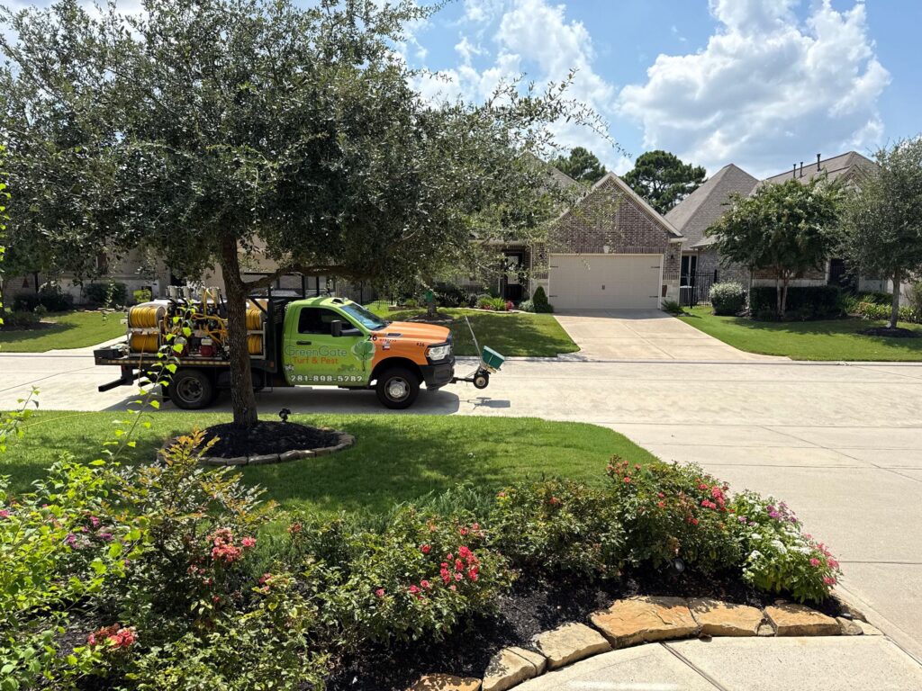 View from the front door, looking at a greengate truck parked on the street in front of a green lawn and flower beds. Just received a sod web worm treatment