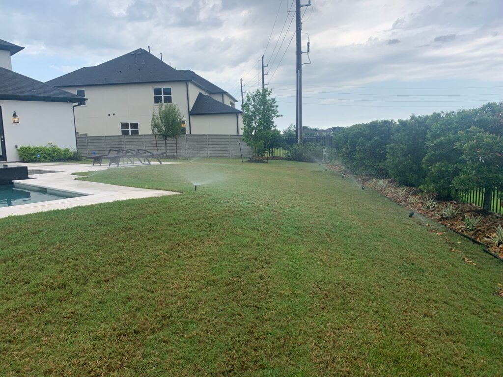 Sprinklers running in a backyard near a pool by a sprinkler repair company